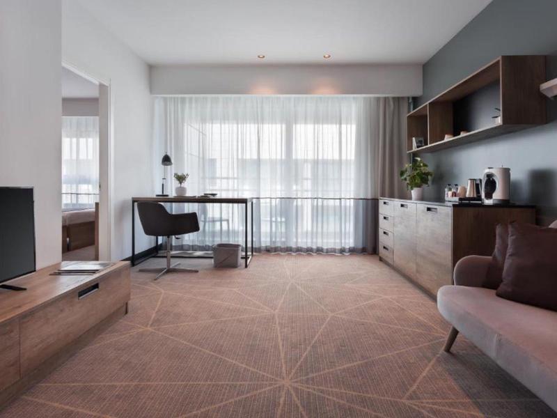 Helles Hotelzimmer mit Schreibtisch, Stuhl und großer Fensterfront mit Blick nach draußen.