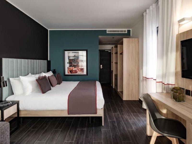 Modernes Hotelzimmer mit großem Bett, Schreibtisch, Fernseher und dunklem Holzboden.