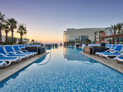 Schwimmbad mit blauen Liegestühlen und Palmen bei Sonnenuntergang