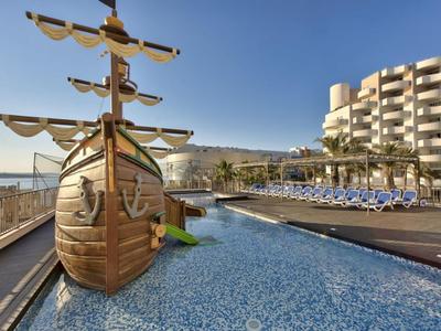 Bazén s dřevěnou lodí a lehátky před hotelem u moře