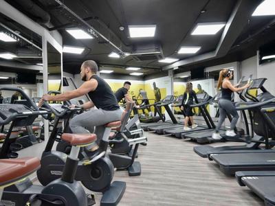 Several people are working out in a modern gym with bikes and treadmills.