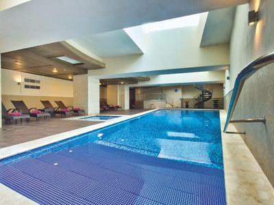 Moderní krytý bazén s modrými lehátky a střešním oknem v lázeňské oblasti.