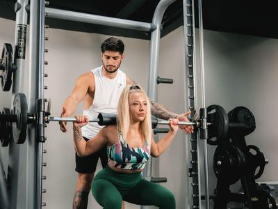 Een man helpt een vrouw bij het squatten in een moderne sportschool van een hotel.
