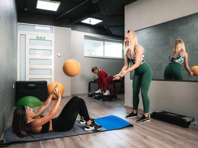 Twee vrouwen sporten in een hotelgym met ballen en matten, spiegel op de achtergrond.