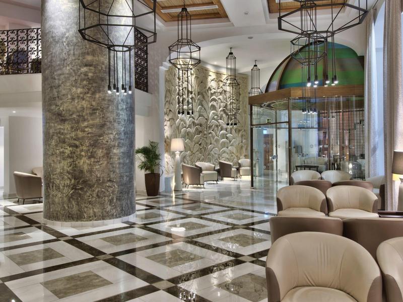 Luxusní hotelová hala s mramorovou podlahou, moderními křesly a velkými sloupy.