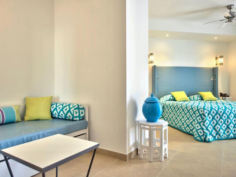 Moderně zařízený hotelový pokoj s modrými a zelenými akcenty a útulným posezením.