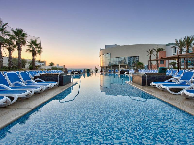 Bazén s modrými lehátky a palmami při západu slunce