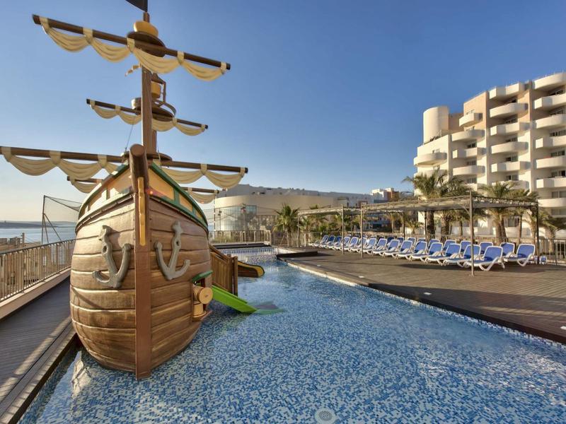 Bazén s dřevěnou lodí a lehátky před hotelem u moře