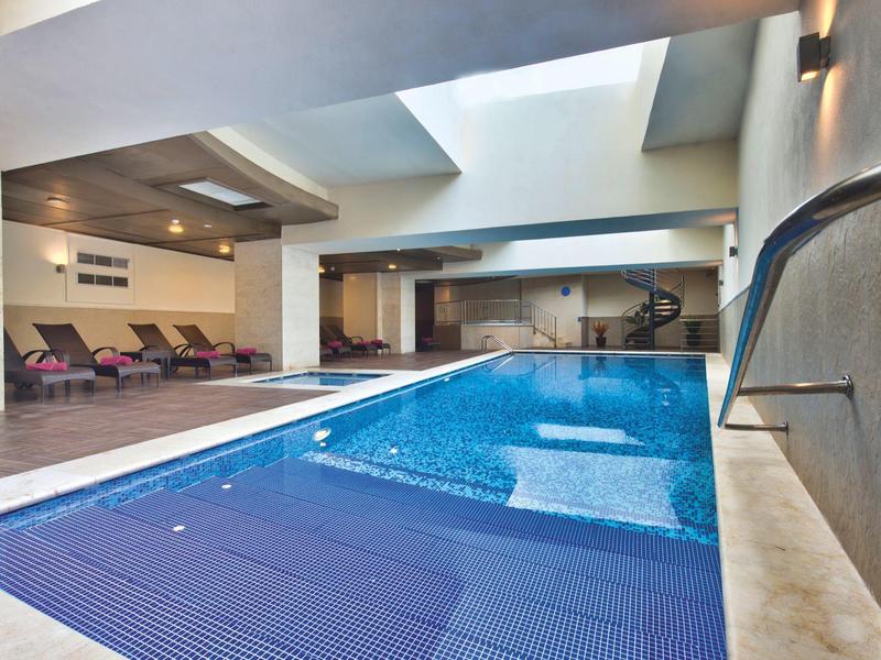 Vnitřní hotelový bazén s lehátky a moderním designem.