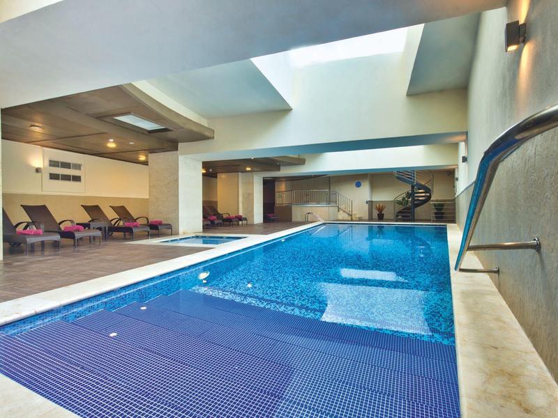 Moderní krytý bazén s modrými lehátky a střešním oknem v lázeňské oblasti.