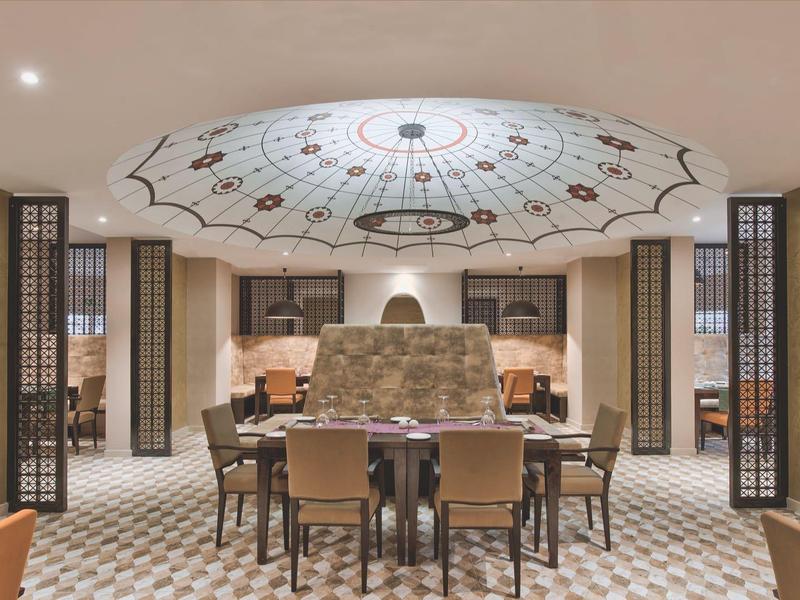 Elegantní jídelna s velkým stolem, židlemi a dekorativním stropem za teplého osvětlení.