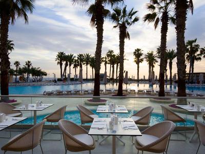 Terrasse eines Restaurants mit Blick auf einen Pool und Palmen bei Sonnenuntergang