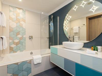 Baño moderno con bañera, espejo redondo iluminado y lavabo sobre mueble colorido.