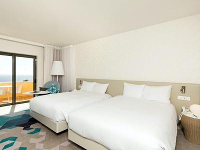 Habitación de hotel moderna con dos camas grandes, balcón con vista al mar y decoración elegante.