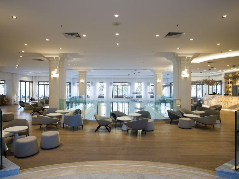 Interior moderno de hotel con piscina, áreas de descanso y luminarias brillantes.