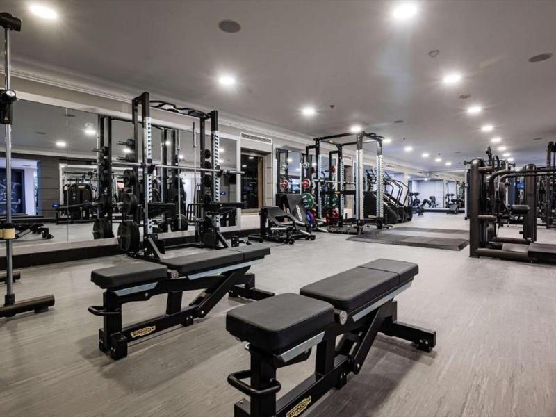 Gimnasio moderno con espejos, pesas y máquinas de ejercicio en una sala luminosa.