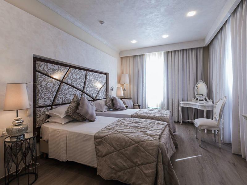 Nowoczesny pokój hotelowy z podwójnym łóżkiem, stolikami nocnymi i dużym oknem z zasłonami.