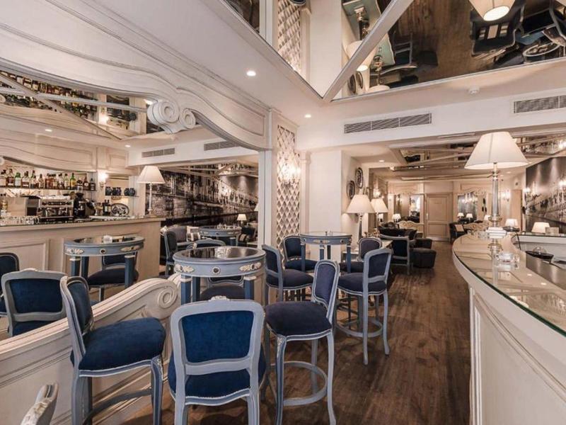 Elegancka restauracja hotelowa z białymi meblami, niebieskimi poduszkami i ciepłą drewnianą podłogą.