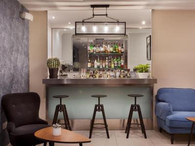 Nowoczesna część baru hotelowego z trzema stołkami barowymi, wygodnymi fotelami i dekoracyjnym lustrem.