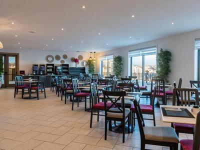 Jasna, nowoczesna restauracja z drewnianymi krzesłami i dużymi oknami wpuszczającymi naturalne światło.