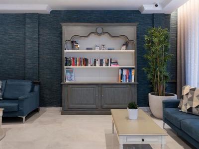 Pohodlný obývací pokoj s modrými pohovkami, knihovnou a rostlinou vedle okna se závěsy.