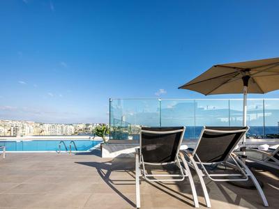 Schwimmbadterrasse mit Sonnenliegen, Sonnenschirm und Blick auf die Stadt bei klarem Himmel.