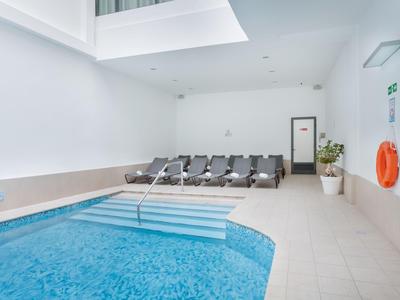 Innenhallenbad mit blauen Fliesen, Treppe, Liegestühlen und Notfallgeräten.