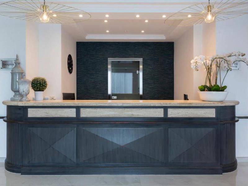 Nowoczesna recepcja hotelowa z czarnym kontuarem, białymi ścianami i roślinami.