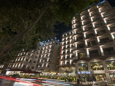 Edificio dell'hotel illuminato di notte con alberi in primo piano e scie luminose di veicoli.