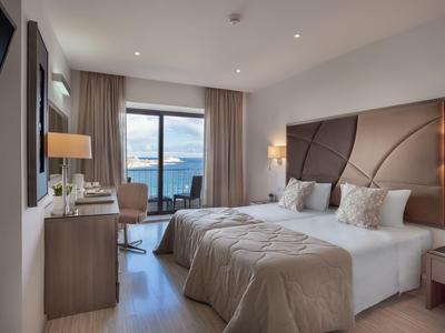 Camera d'hotel moderna con letto matrimoniale, scrivania, balcone e vista sul mare.