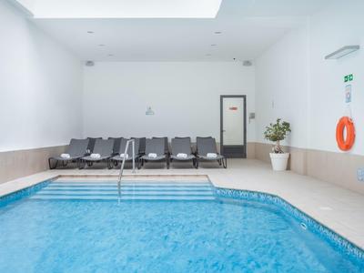 Area piscina interna con acqua blu, sedie nere e pareti bianche