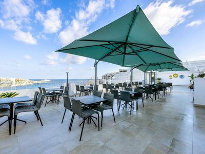 Freiluftrestaurant mit blauen Sonnenschirmen und Blick auf das Meer bei klarem Himmel.