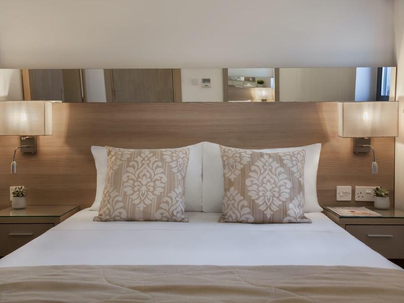 Camera moderna con letto matrimoniale, cuscini decorativi e comodini con lampade.