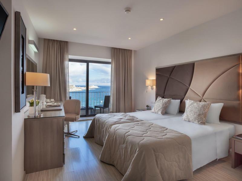 Camera d'hotel moderna con letto matrimoniale, scrivania, balcone e vista sul mare.