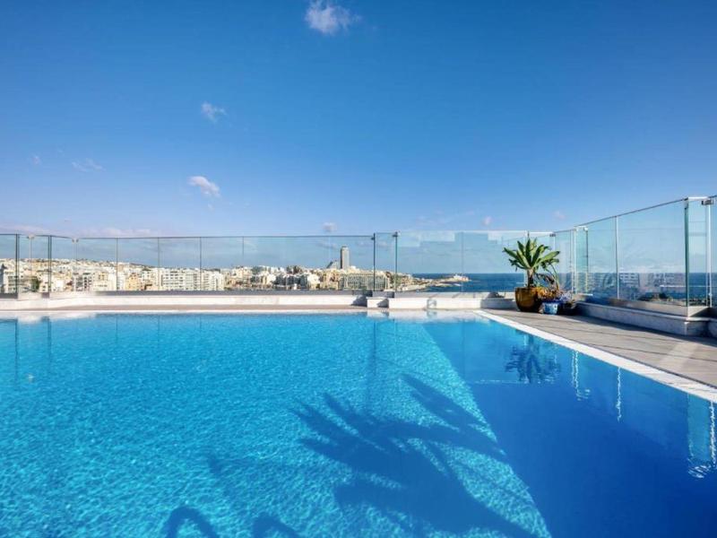 Piscina sul tetto con vista sulla città sotto un cielo blu limpido.