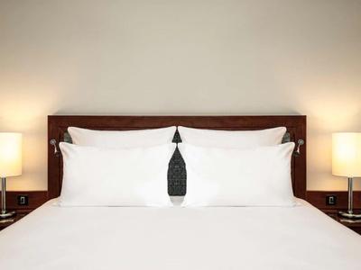 Weißes Bett mit vier Kissen, dunklem Holzkopfteil und zwei Nachttischlampen auf beiden Seiten.