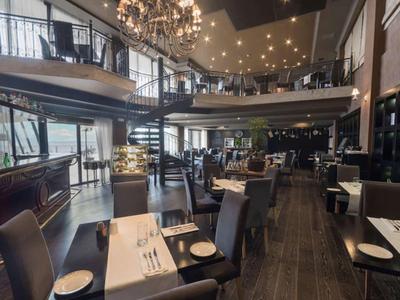 Modernes Restaurant mit dunklen Holzmöbeln, eleganten Deckenleuchten und großzügigem Raumangebot.