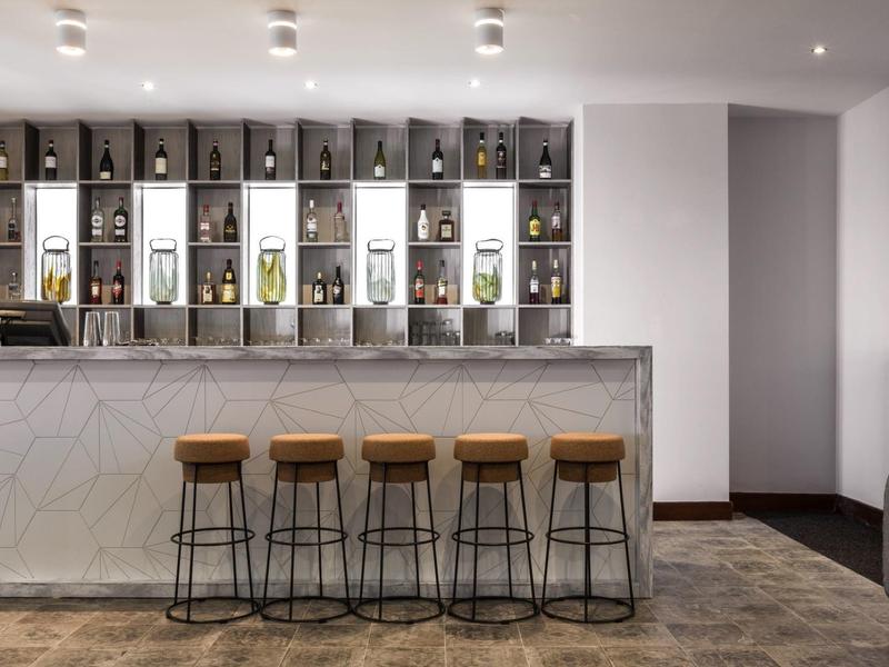 Moderní bar s mramorovým pultem a čtyřmi stoličkami před regálem s lahvemi.