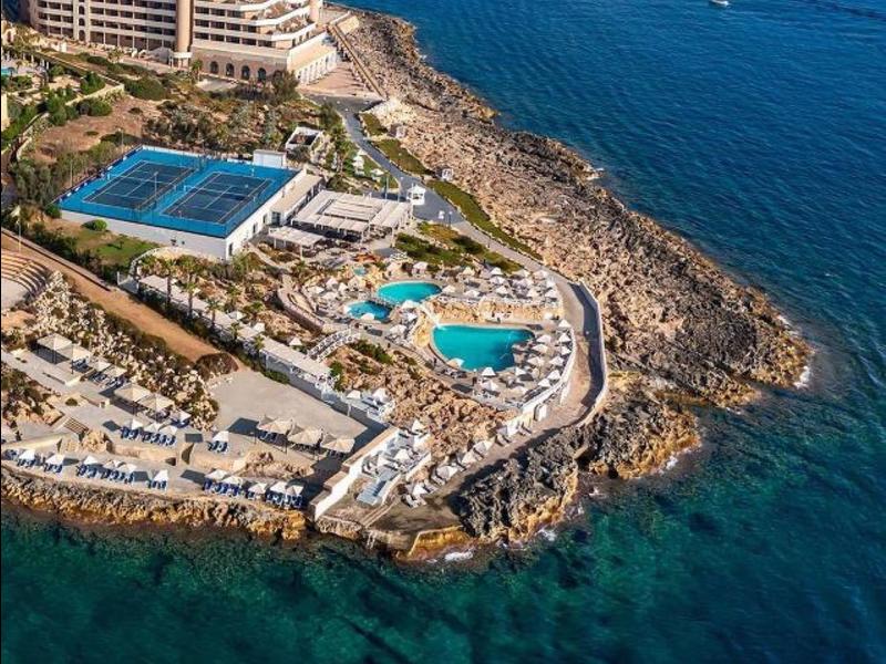 Luxusní hotel na skalnatém pobřeží s bazény a výhledem na modré moře.