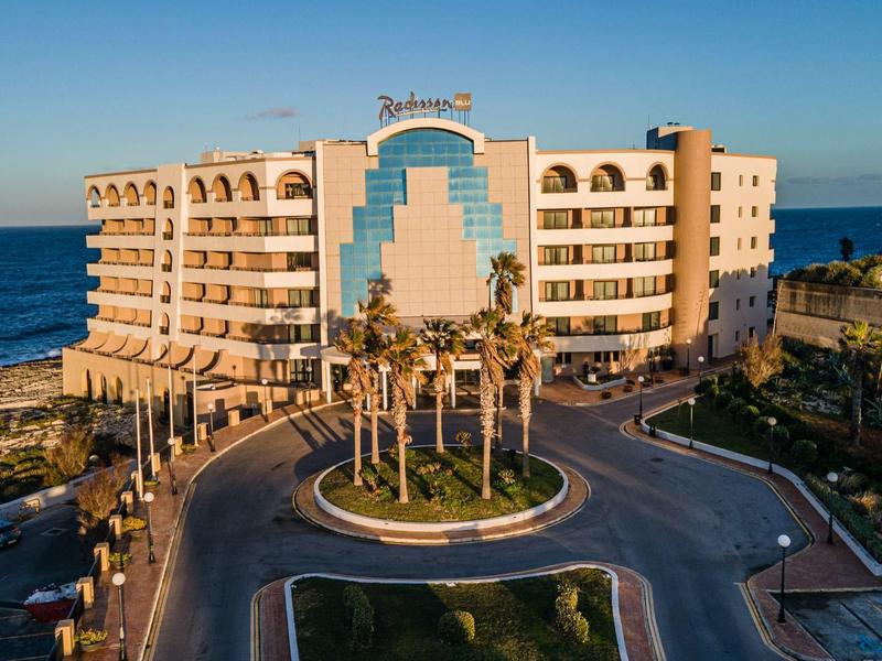 Moderní hotelová budova na pobřeží s palmami a výhledem na moře za jasné oblohy.