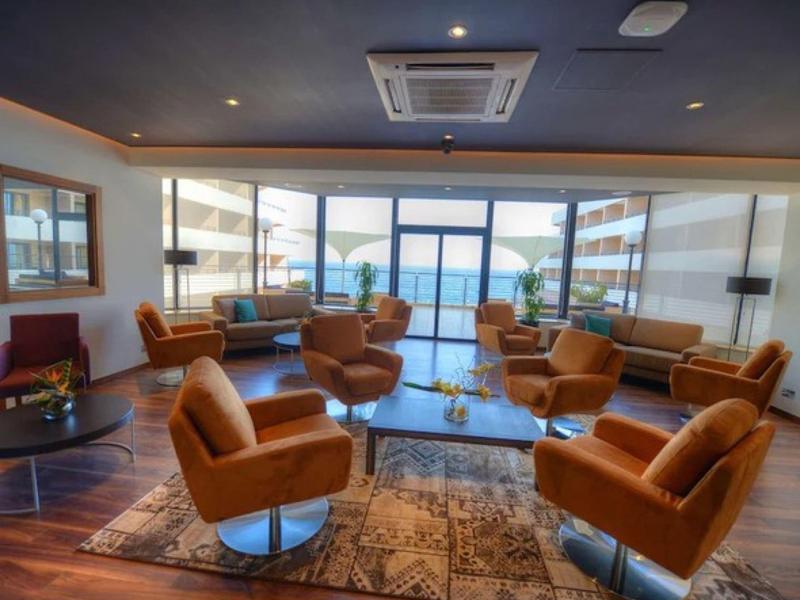 Světý obývací pokoj s hnědými křesly, kobercem a výhledem na balkon a moře.