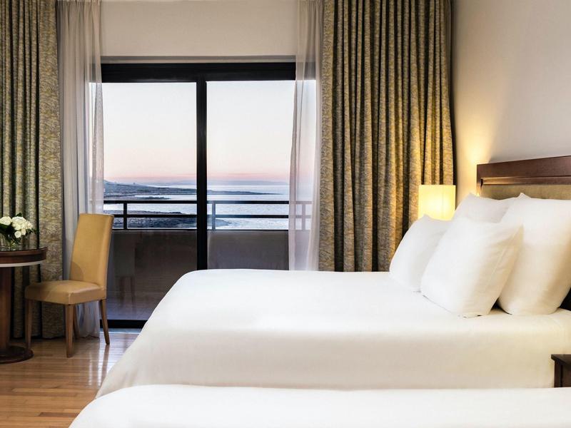 Moderní hotelový pokoj s velkou postelí, balkonem a jemným osvětlením za soumraku.