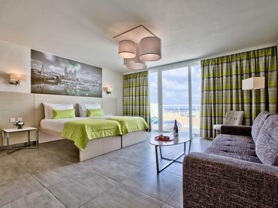 Modernes Hotelzimmer mit Doppelbett, Sofa und großem Fenster mit Vorhängen.