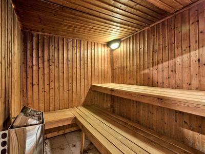 Innenraum einer Sauna mit Holzwänden, Holzbank und Saunaofen in der Ecke.