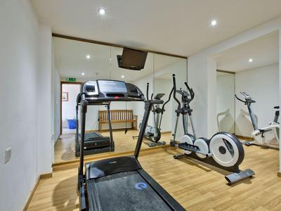 Kleines Fitnessstudio mit Laufband, Crosstrainer und Rudergerät vor Spiegelwand.