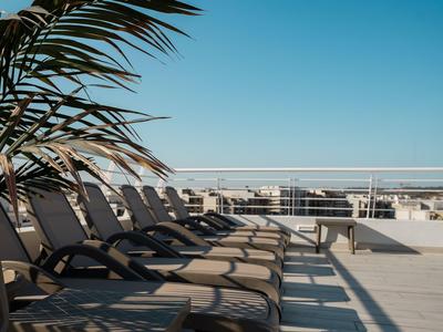 Leerer Liegestuhlbereich mit Palmen auf einer sonnigen Hotelterrasse mit Blick aufs Meer.