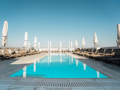 Ein klarer blauer Pool mit Liegestühlen und geschlossenen Sonnenschirmen an einem sonnigen Tag.