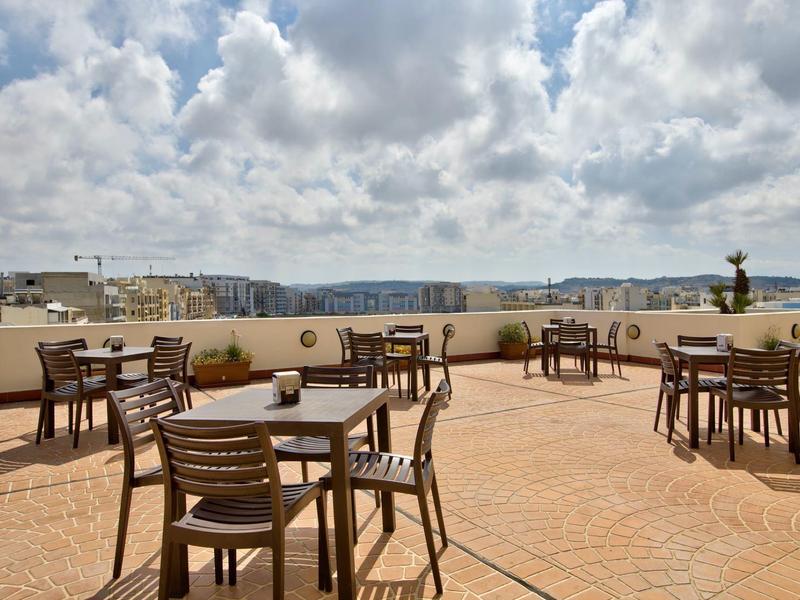 Terrasse sur le toit avec des tables et des chaises en bois sous un ciel nuageux avec vue sur la ville.