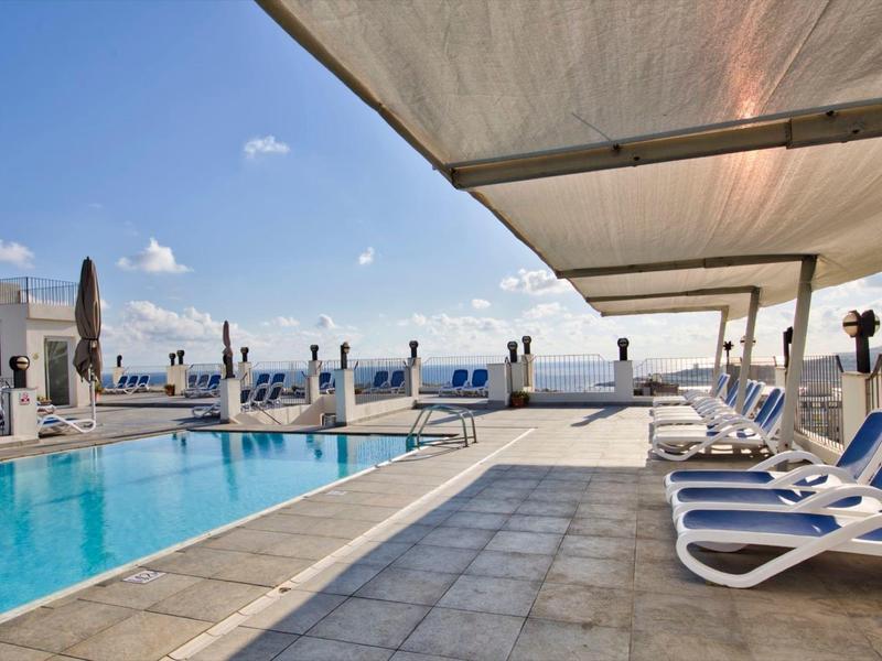 Piscine d'hôtel moderne avec chaises longues et parasols sous un ciel clair.