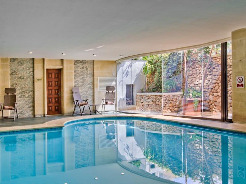 Espace intérieur avec piscine bleue claire, fenêtres en verre et murs en pierre dans un hôtel.